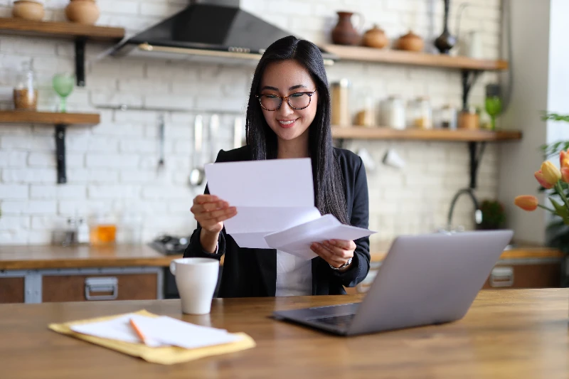 Home 6 Businesswoman happily reads financial letter at a desk with laptop